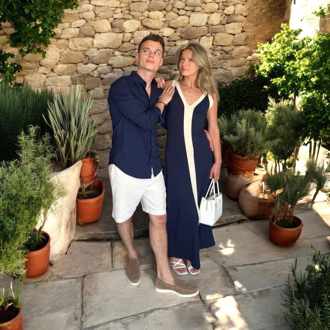 Couple debout dans une cour de pierre fleurie, elle en robe longue bleu marine à bordures blanches, lui en chemise bleu marine et short blanc
