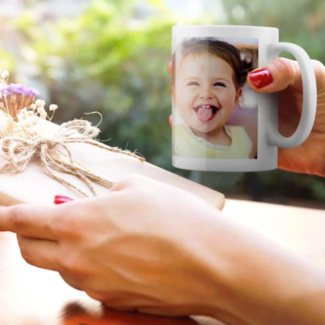 Un mug blanc imprimé d’une photo, tenu en main à l’extérieur