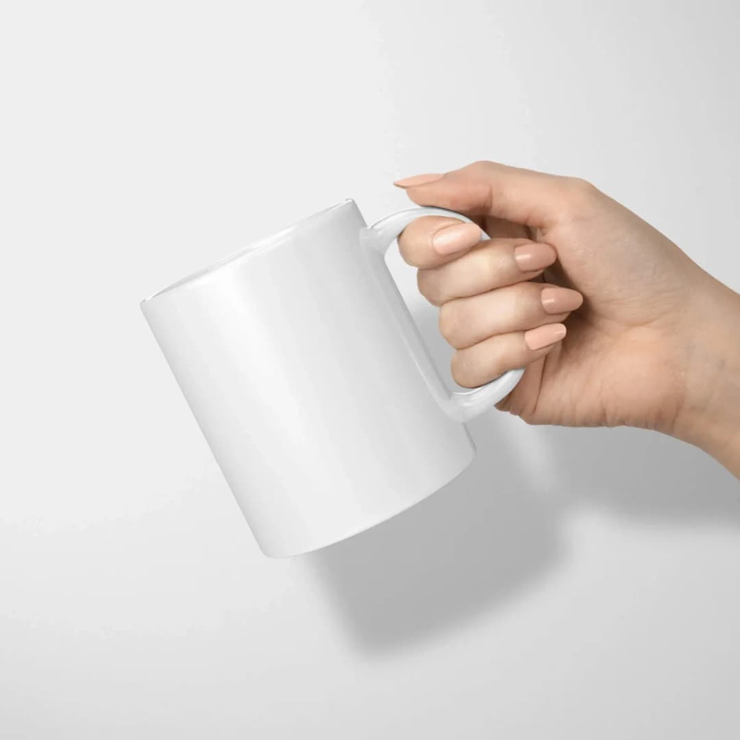 Une main tient par l’anse un mug blanc en céramique, le modèle de 325 ml, sur une photo de présentation